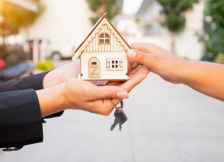 Salesman carrying a model house in hand is delivering the house key to the buyer