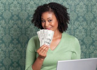 Woman holding currency in front of laptop - stock photo
