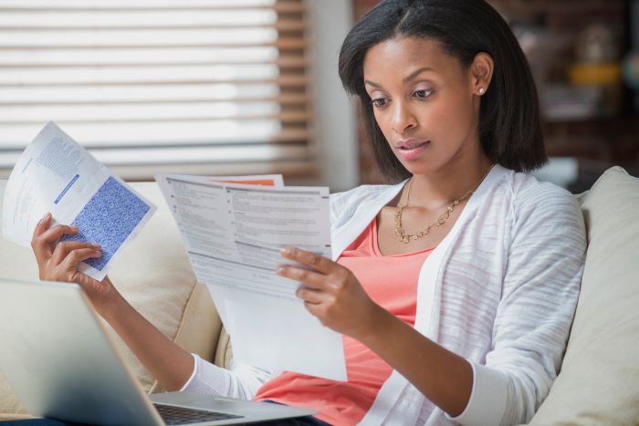 Mixed race woman reading bills on sofa - stock photo