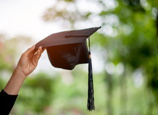 Close-Up Of Cropped Hand Holding Mortarboard Against Blurred Background