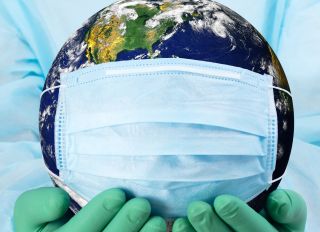 Pandemic concept - doctor's hands in gloves holding the planet Earth in a medical mask - stock photo