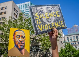 A Silence Is Violence sign in front of a portrait of George...