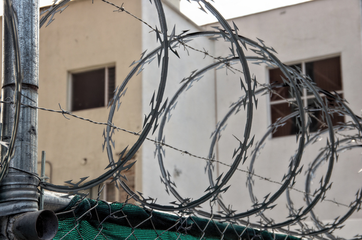 Razor wire and barbed wire across the top of a wire mesh security gate around a building