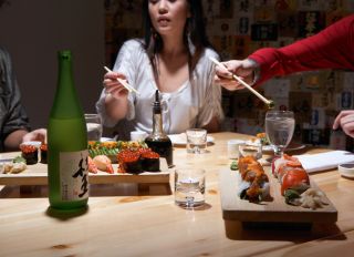 Three young women eating sushi in restaurant, mid section