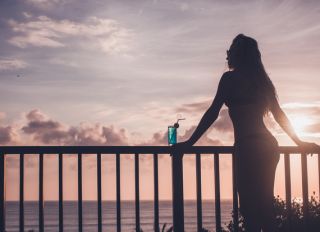 Silhouette of sensual woman drinking blue lagoon cocktail on tropical balcony at sunset.