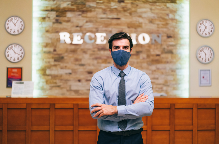 Manager of a luxury hotel wearing protective face mask with arms crossed, during Covid tourism and hotel reopening