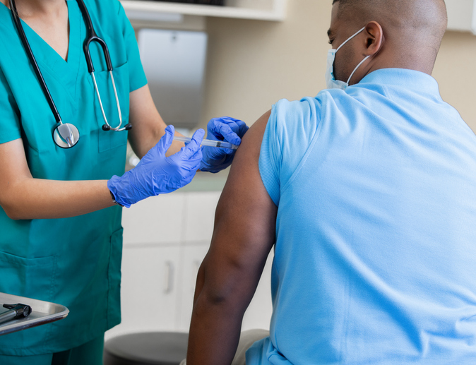 Nurse gives mature African American man a vaccination in doctor's office during coronavirus pandemic