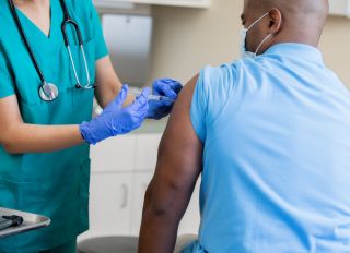Nurse gives mature African American man a vaccination in doctor's office during coronavirus pandemic