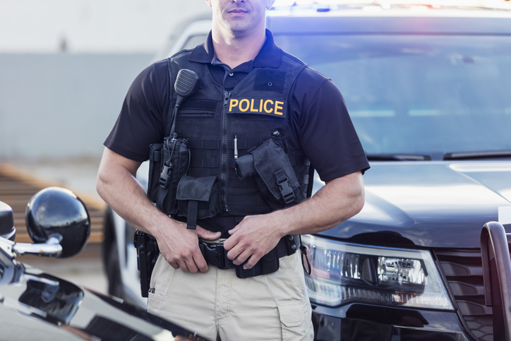 Policeman wearing bulletproof vest, by patrol car