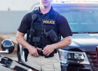 Policeman wearing bulletproof vest, by patrol car