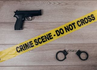 Crime scene tape, handcuffs and gun on wooden background