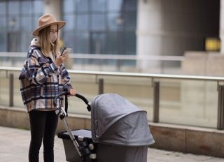Happy Mother Walking With Stroller In Park And Using Mobile Phone. Joy Of Motherhood. Stylish Woman