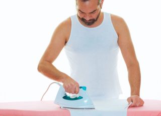Man ironing undershirt against white