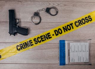 Crime scene tape, handcuffs and gun on wooden background