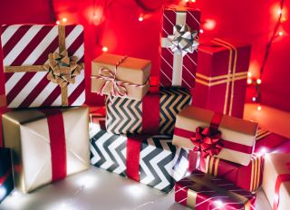 Stack of present boxes wrapped in ornamental paper and illuminated with fairy lights on Christmas day against red background. New Year celebration concept