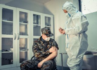 Doctor wearing protective work wear injecting COVID-19 vaccine to soldier