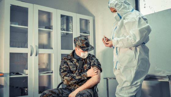 Doctor wearing protective work wear injecting COVID-19 vaccine to soldier