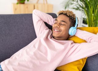 Teenage boy enjoying listening music while relaxing lying on a couch at home.