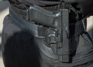 A Glock pistol seen in close-up hanging from the belt of a...
