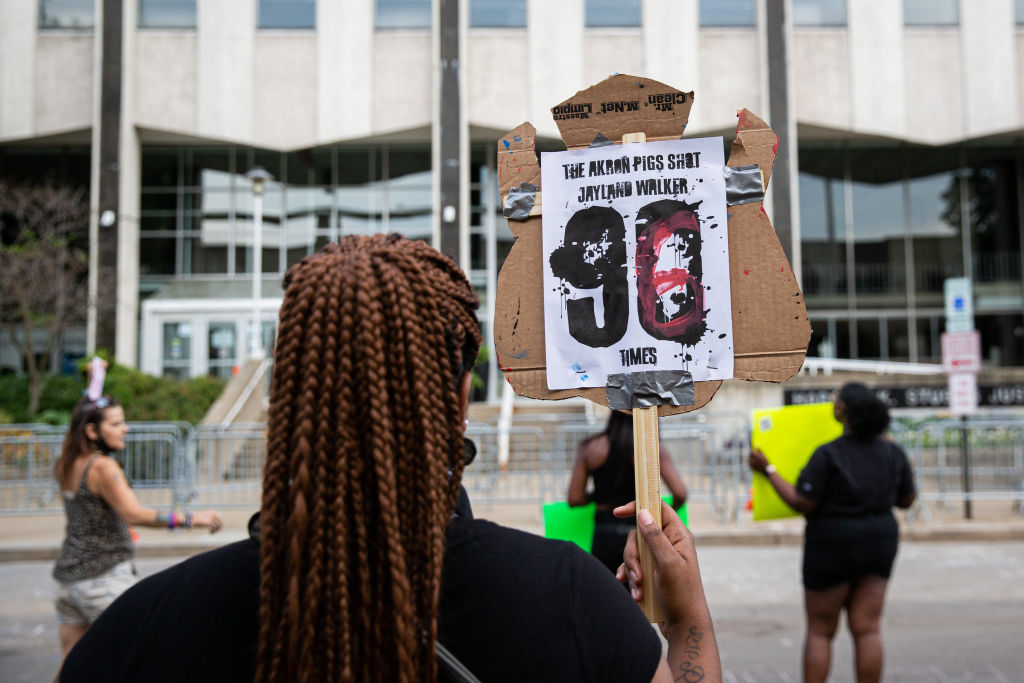A protester holds a sign that says, "The Akron pigs shot...