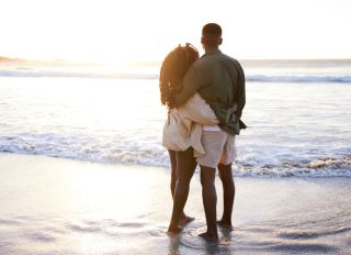 Young couple standing arm in arm on a beach and watching the sunset