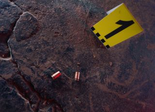 Two illuminated bullet casings on a black stoned floor and a forensic scientist's number next to it in close up, macro photo