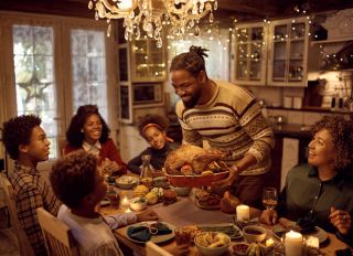 Happy African American man serving stuffed turkey while having dinner with his extended family in dining room on Thanksgiving.