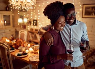 Embraced African American couple drinking while celebrating Thanksgiving at home.