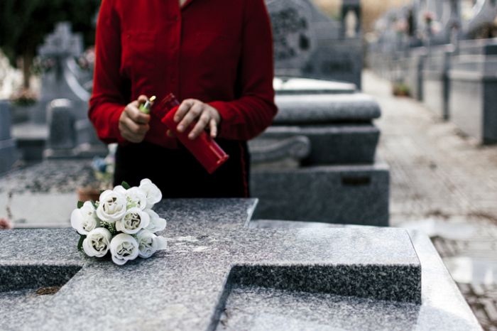 Woman in red blouse lighting a candle and putting flowers to a loved one in the cemetery.