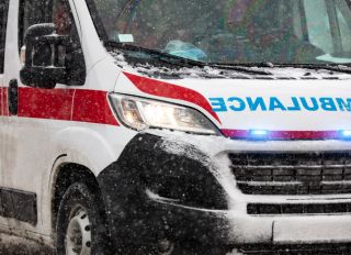 911 ambulance van rushing through traffic during heavy winter snowfall conditions.