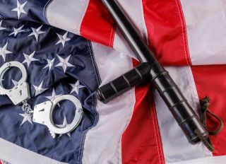 silver metal handcuffs and police nightstick over US flag on flat surface