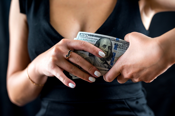young girl eagerly counts dollars money in black dress isolated on black background.