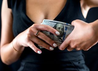 young girl eagerly counts dollars money in black dress isolated on black background.