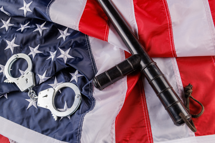 silver metal handcuffs and police nightstick over US flag on flat surface
