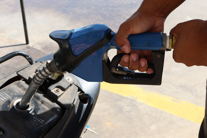 Detail of the hands of a black gas station attendant fueling a motorcycle