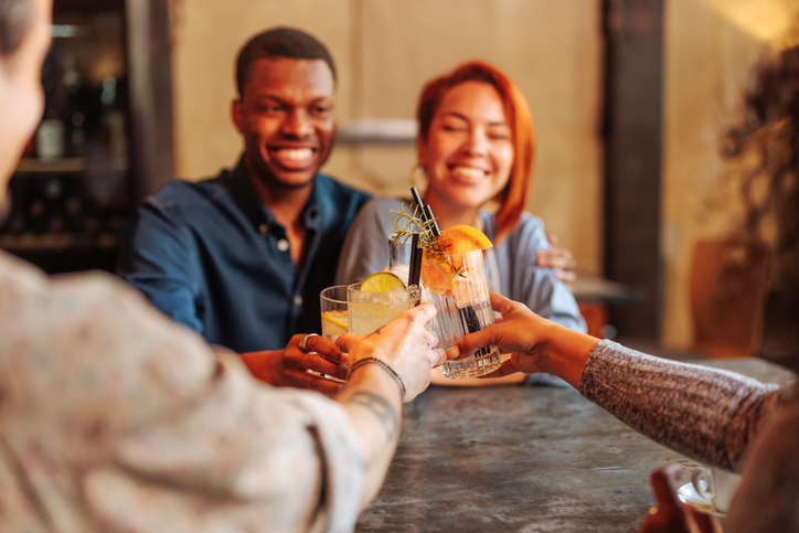 Father's Day - Young African-American man and Hispanic woman toasting cocktail glasses with friends in restaurant.