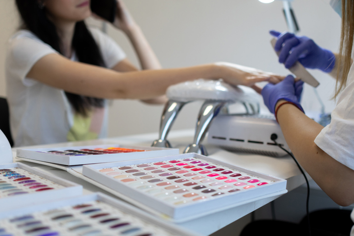 Young woman on manicure treatment in beauty salon. Professional nail care and painting in modern beauty nail salon. UV lamp gel polish manicure process.