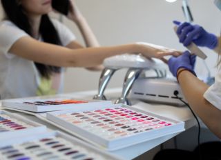 Young woman on manicure treatment in beauty salon. Professional nail care and painting in modern beauty salon. UV lamp gel polish manicure process.