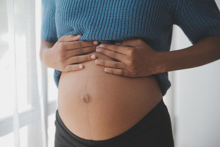 Happy pregnant woman touching belly in front of white wall