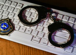 Concept of cybercrime and cybersecurity with keyboard, handcuffs, and police badge