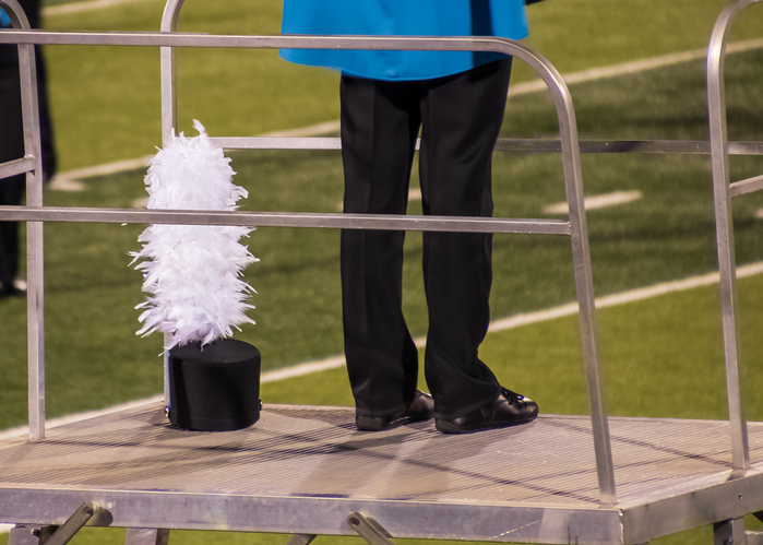 High school marching band conductor stands on metal lift with shako hat with plumes