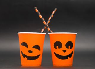 Halloween coffee paper cup with pumpkin faces on black background. Concept for coffee house