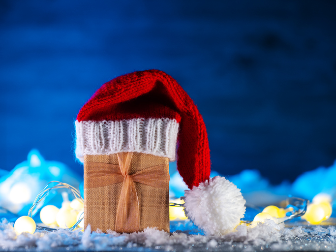 A Christmas gift in a Santa hat on a snow table. Blue background, copy space