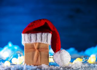 A Christmas gift in a Santa hat on a snow table. Blue background, copy space