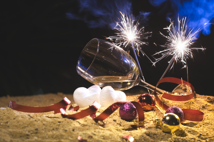 NYE - Wine glasses and firework on the beach, party celebration, valentine's day with red confetti and white heart shape on sand beach. After party outdoor chaos. Party invitation concept.