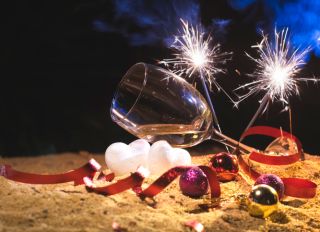 Wine glasses and firework on the beach, party celebration, valentine's day with red confetti and white heart shape on sand beach. After party outdoor chaos. Party invitation concept.