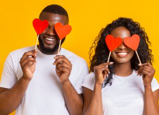 Cheerful black couple covering eyes with red heart paper cards - stock photo