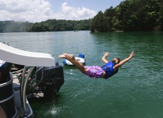 Child sliding off pontoon boat slide into lake on belly
