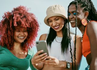 Shot of a group of young friends using a phone in the city - stock photo