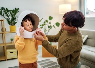 Mother and son playing with carboard astronaut helmet at home